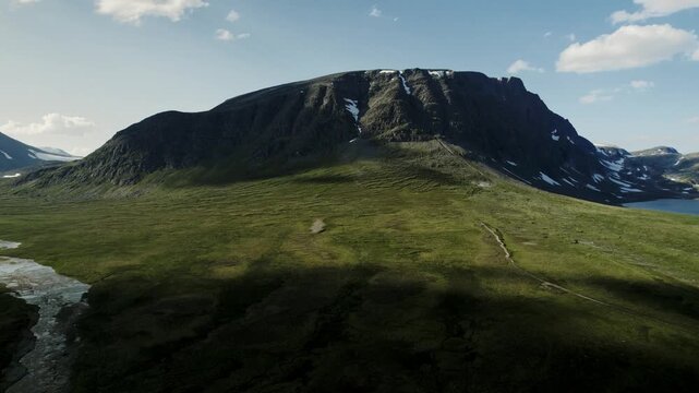 Cinematic drone shot flying sideways and forward towards the massive Blahoa mountain. View of the green tundra and lake Bl&aring;h&oslash;tj&oslash;nna in the Trollheimen range, Oppdal, Norway. Sunny summer day