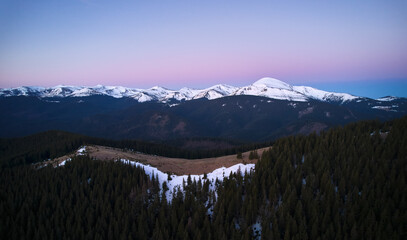 Naklejka premium Beautiful panorama of mountains with spruce trees and hills covered with snow under sunset sky