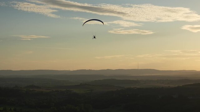 Paramotor flies over Moselle hills at sunset in golden haze