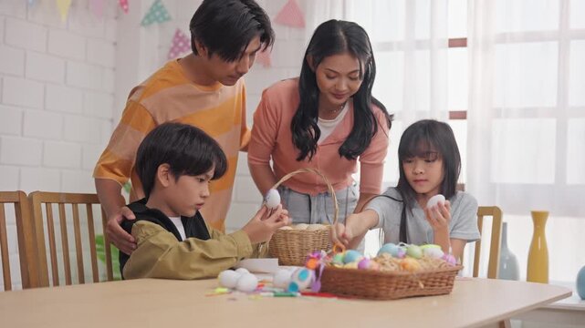 Asian young children and parents coloring Easter eggs on table in house. 