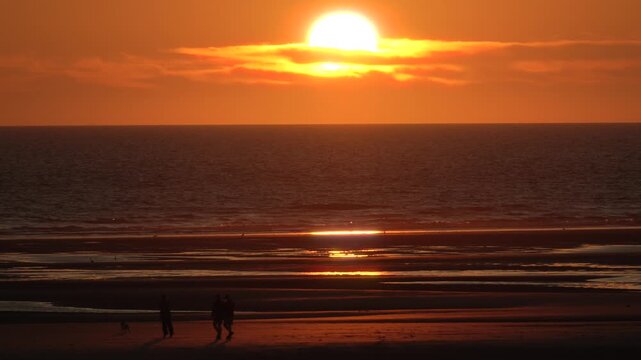 People walk along Opal Coast beach at sunset with golden reflections