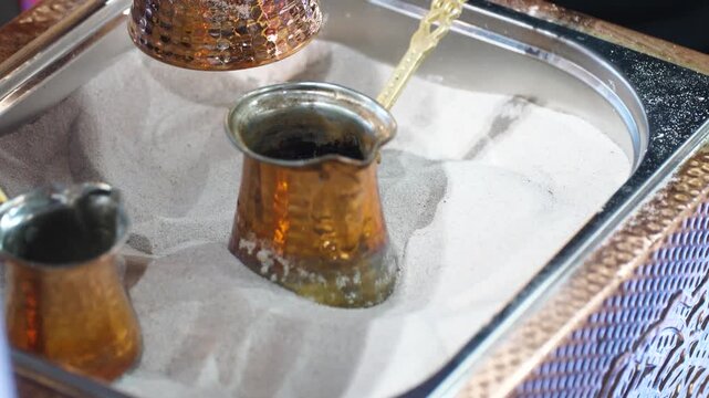Static close up of a traditional hammered copper pot sitting in hot sand. Preparation of authentic oriental coffee using ancient heating technique in a middle eastern cafe.