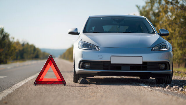 car on the road, The vehicle appears to have a breakdown, Emergency signaling is visible in the foreground, A warning sign alerts oncoming traffic, The driver is experiencing technical issues