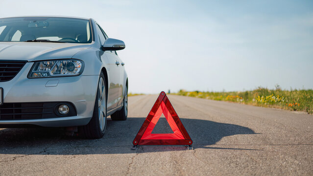 car crash, ​An orange warning triangle stands on the ground, The vehicle has broken down, It is a typical roadside emergency scene, The car is waiting for a tow truck, Hazard signs are visible