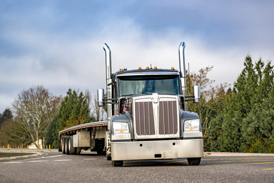 Black day cab bonnet big rig semi truck with empty flat bed semi trailer driving on the round road intersection