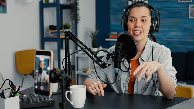 Famous influencer streaming remote podcast using smartphone while talking to audience. Attractive online live radio talk show host discussing last worldwide news and evens with public.