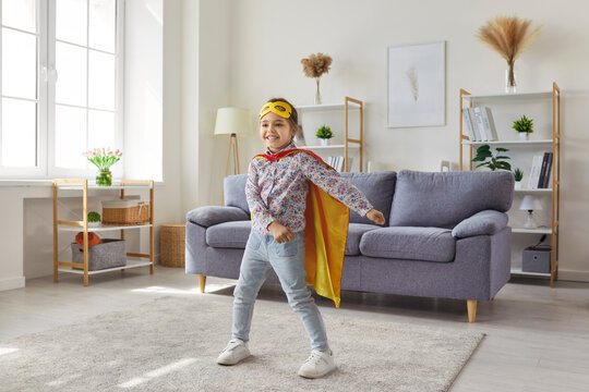 Superhero girl playing, active fun game of happy child in costume and mask of leader in living room. Preschool excited kids dreams of super hero power and courage. Childhood, imagination concept