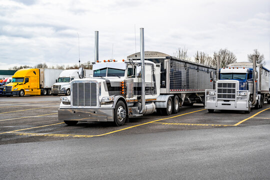 Two classic bonnet big rig semi trucks with loaded bulk semi trailers standing on the reserved parking spots on the truck stop taking break