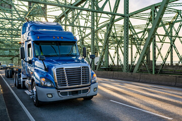 Popular low cab profile blue big rig semi truck with flat bed semi trailer running on the truss...