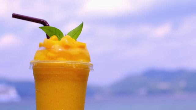 Smoothie made from fresh mango fruits against the backdrop of a seascape. Fruit and yoghurt ice cream decorated with leaves. Glass of tropical dessert close-up.