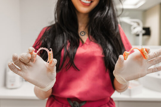 Dental professional in clinic wearing medical gloves, holding and presenting two types of removable partial dentures