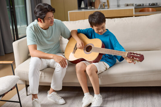 A boy plays guitar next to his dad