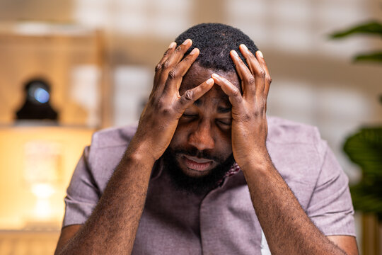 African man closing eyes, holding head in pain, feeling frustrated and stressed