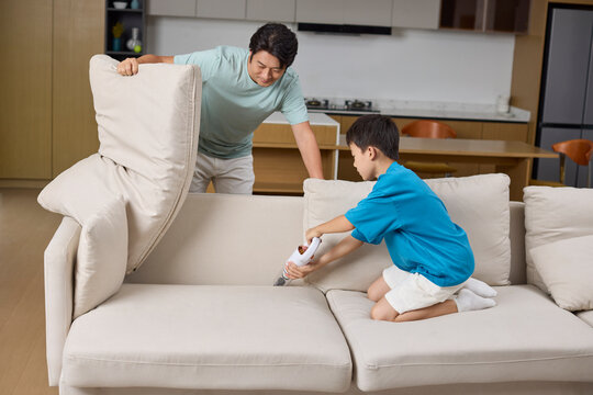 Happy dad and son team up to tackle the sofa with the vacuum cleaner