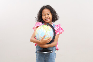 Fototapeta premium A little Asian girl holding a globe during geography lesson, concept of earth day or preserving the earth's sustainability and ecosystem, isolated on grey background.