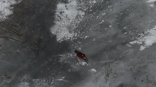 Drone top view with camera zooms in of woman hunter lying on frozen lake with eagle owl