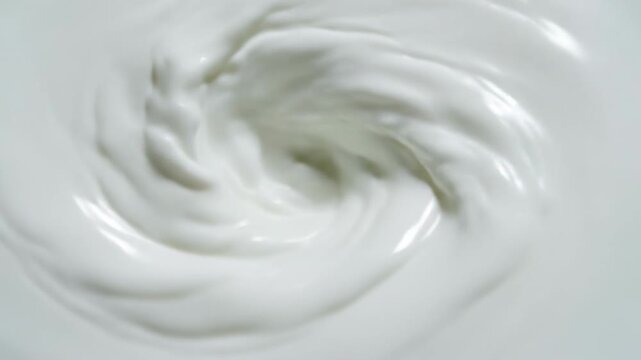 White creamy substance swirling in a circular motion, showcasing the dynamic flow and texture of the mixture in a close-up view, emphasizing its smooth consistency