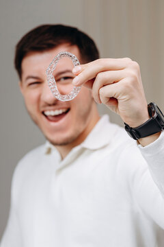 Young man holding a clear aligner tray while smiling to showcase invisible orthodontic dental treatment