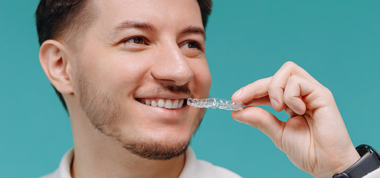 Young man smiling while holding a clear dental aligner for orthodontic teeth straightening