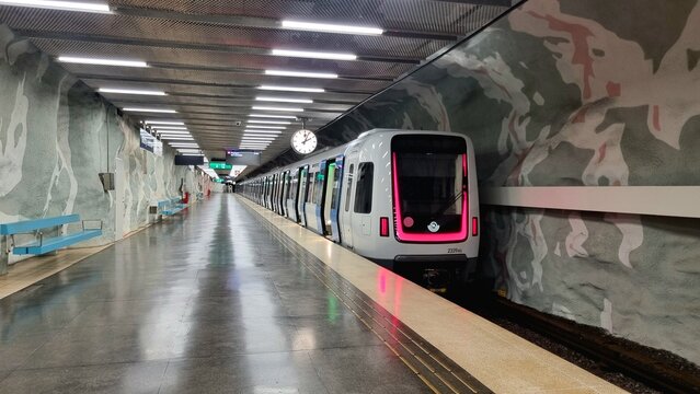 Stockholm, Sweden. 02.27.2026.  Stockholm metro station with decorative patterned walls, benches for passengers and stylish clock, metro train with pink backlight, modern metro train approaching