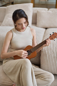 Beautiful woman playing ukelele at home