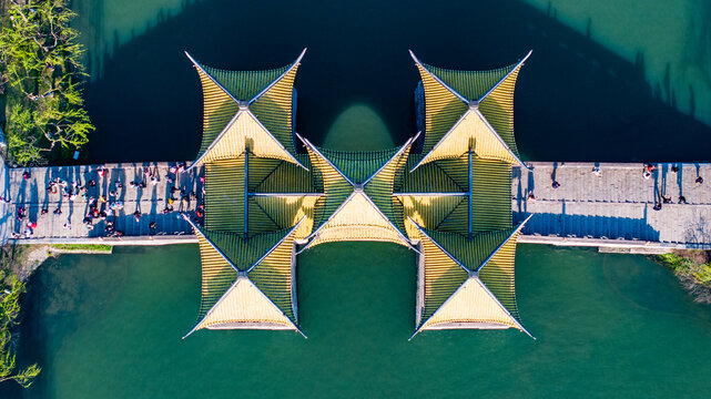 Aerial view of the Five Pavilion Bridge (Wuting Bridge) at Slender West Lake in Yangzhou, China, featuring traditional Chinese architecture, geometric symmetry and tourists crossing over green water