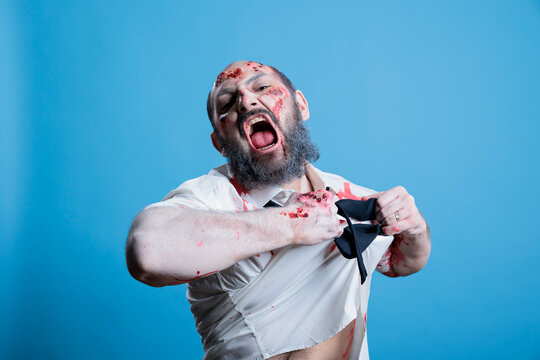 Man raging and ripping clothes in frustration, tired of capitalism rat race overworking turning him into zombie. Employee tearing shirt, quitting stressful job working him to death, studio background