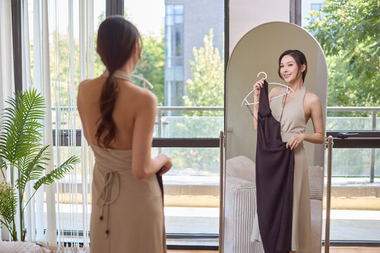 Elegant woman holding a dress and watching her reflection in the mirror