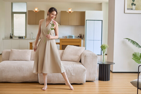 Barefoot and comfortable, a beautiful woman wandering her home, a flower in her hand