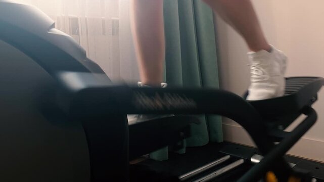 Woman exercising on elliptical trainer at home in sunlight