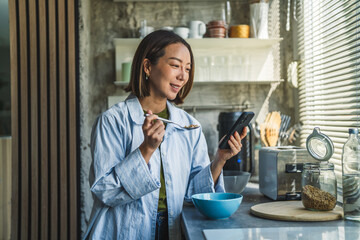 Woman eating breakfast and using smart phone in kitchen