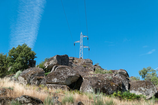 Torre el&eacute;trica de alta tens&atilde;o erguida sobre um afloramento rochoso gran&iacute;tico em meio a uma paisagem &aacute;rida com vegeta&ccedil;&atilde;o rasteira e um c&eacute;u azul