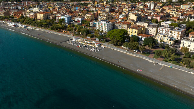 Aerial view on the seafront of Sapri, in province of Salerno, Campania, Italy. Panorama of a beautiful coastal town with colorful buildings, a dark sandy beach, and clear turquoise sea water.