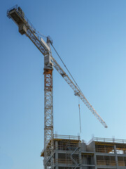 Naklejka premium Tower Crane Above Building Construction Site with Concrete Structure and Clear Blue Sky Background