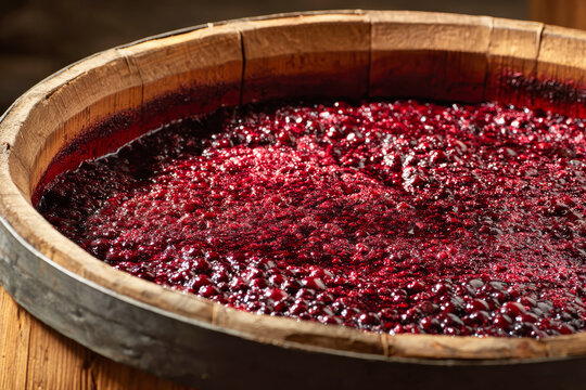 Red grape must sits in an old wooden barrel with a half-open lid as it undergoes fermentation for traditional wine production in a winery