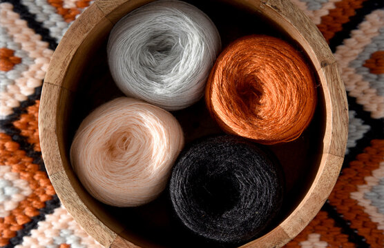 Top view of yarn balls in wooden bowl and vintage scissors on bargello needlepoint blanket, colorful wool thread for embroidery, cozy handmade geometric flame stitch craft background