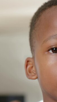 Vertical video: Blinking then tilting right-half boy's face forming smile home TV left, copy space