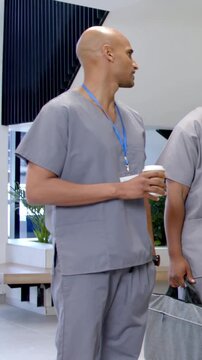 Vertical video: After glance staff in grey scrubs blue ID holding coffee, chatting on break in hall