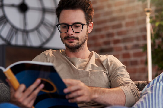 Portrait of man sitting on couch at home reading a book