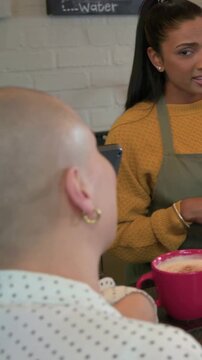 Vertical video: Starting, barista in apron clarifying at counter while customer turning, pink mug