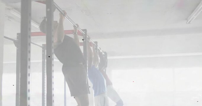 Three men reaching up and gripping rig, backlit gym, doing pull-up reps for strength ending hang
