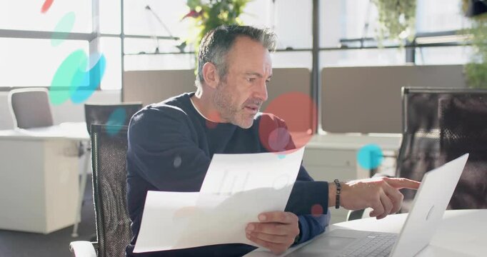 Man holding two sheets, comparing charts to laptop, generating floating graphs for finance review