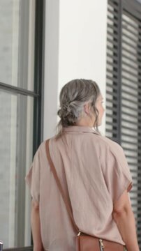 Vertical video: Entering woman wearing pink top turning and walking into home, holding hat with bag