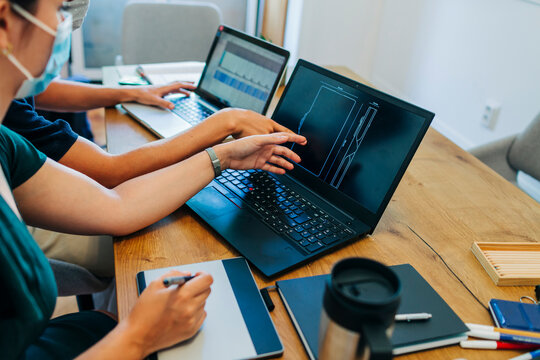 Programmers discussing over laptop while wearing protective face mask at office during coronavirus