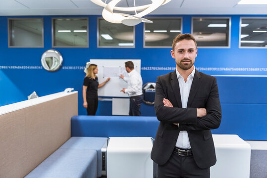 Businessman standing in conference room, while colleagues working with flipchart in background