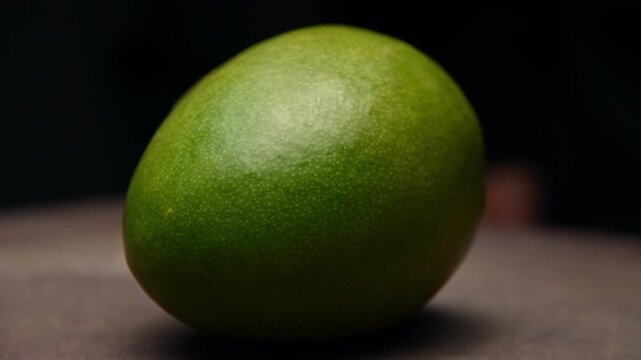 Green mango resting on a textured surface with dark background, close-up view