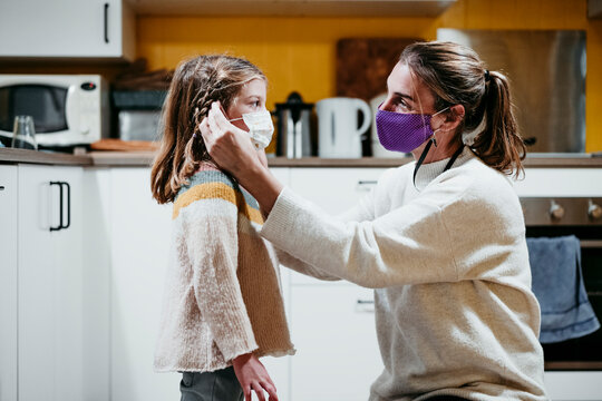 Mother adjusting daughter face mask while sitting at home