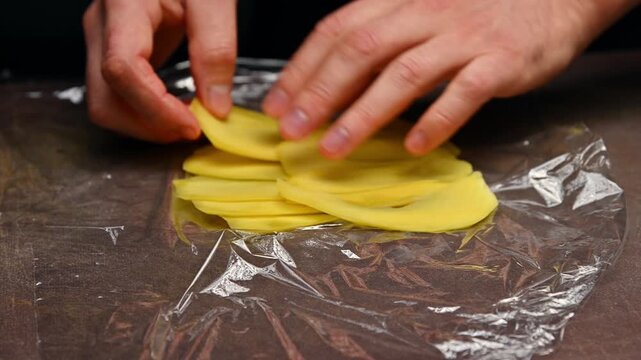 Hands preparing yellow mango slices on plastic wrap for culinary presentation