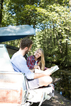 Smiling young couple with map and canoe in car at a brook