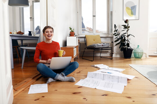 Woman sitting cross-legged on floor of her home, using laptop